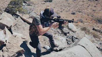 Man in airsoft gear crouched aiming an airsoft rifle